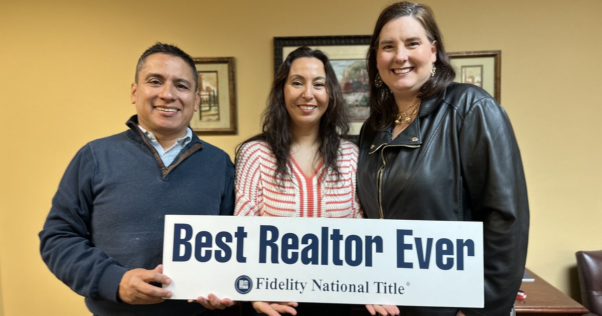 Lisa Collio posing with a smiling couple at a title office, the three of them holding a white sign.