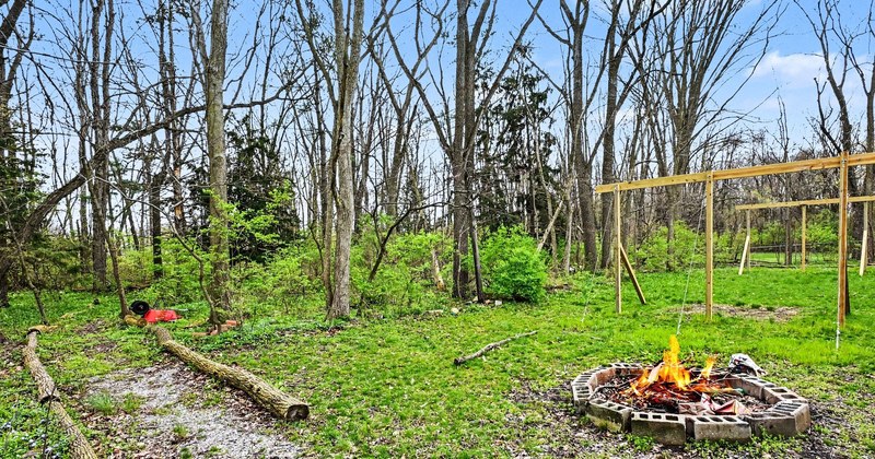 A wooded backyard with a swing set and fire pit.