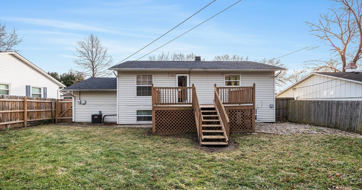 The rear of a home with deck stairs and a fenced yard.