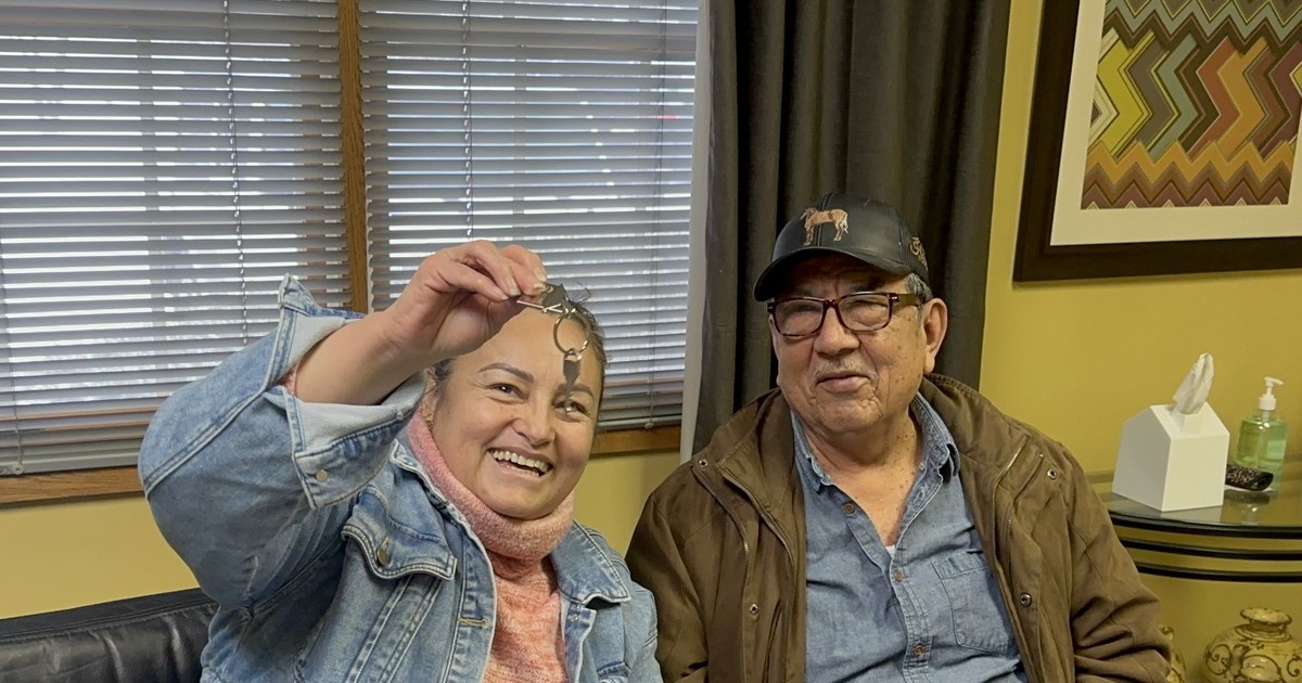 Two smiling people at a conference table, one holding up a house key.