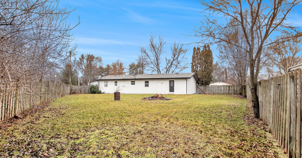 The rear yard of a ranch home with a leafy lawn and wooden fence.