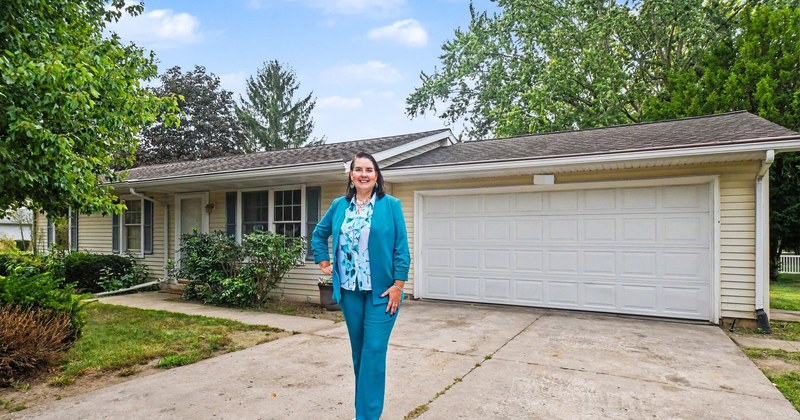 Lisa Collio smiling in a teal suit in front of a single-story house with a two-car garage.