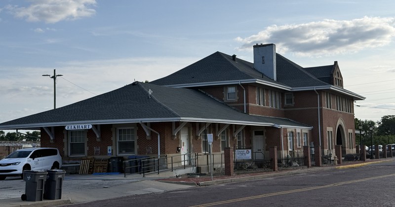 Una estación de tren de ladrillo de una planta, con un alero amplio y la palabra ELKHART sobre la marquesina, junto a una calle vacía.