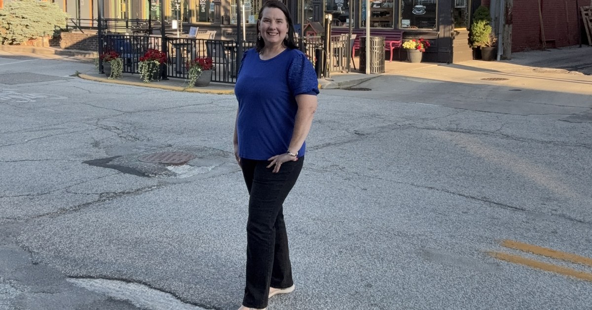 Lisa Collio standing on a downtown Goshen street corner, with a restored Victorian storefront and outdoor seating behind her.