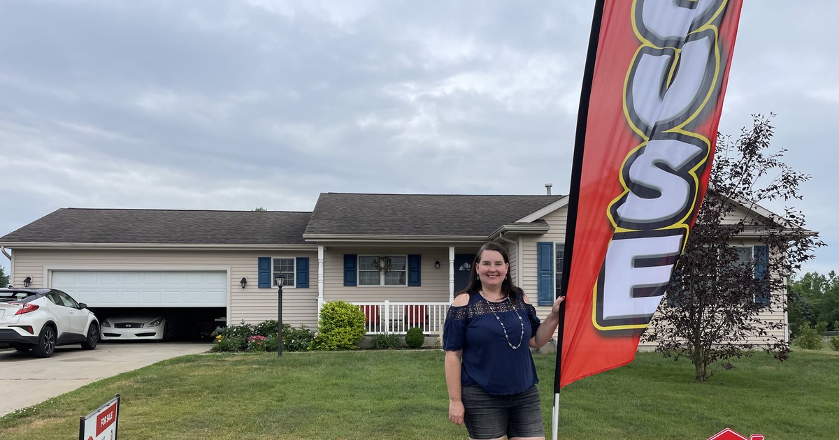 Lisa Collio standing beside an open-house flag in front of a home.