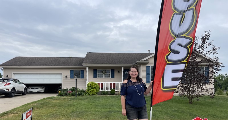 Lisa Collio standing beside an open-house flag in front of a home.