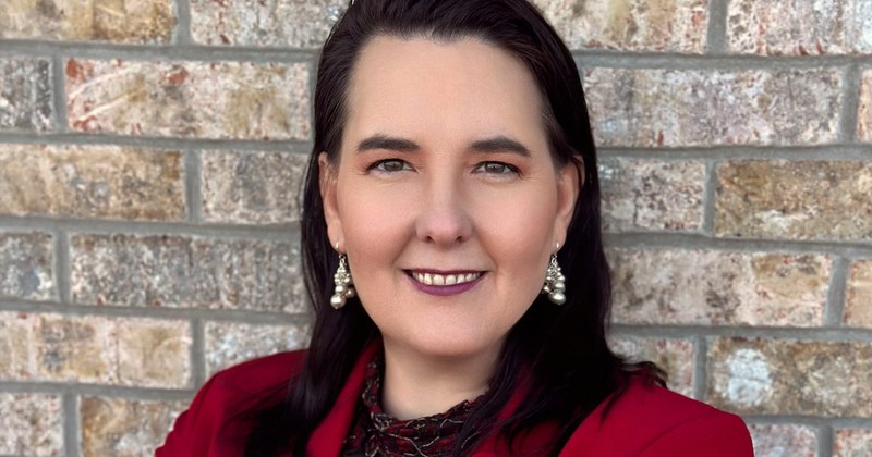 Lisa Collio in a red blazer standing by a brick wall.