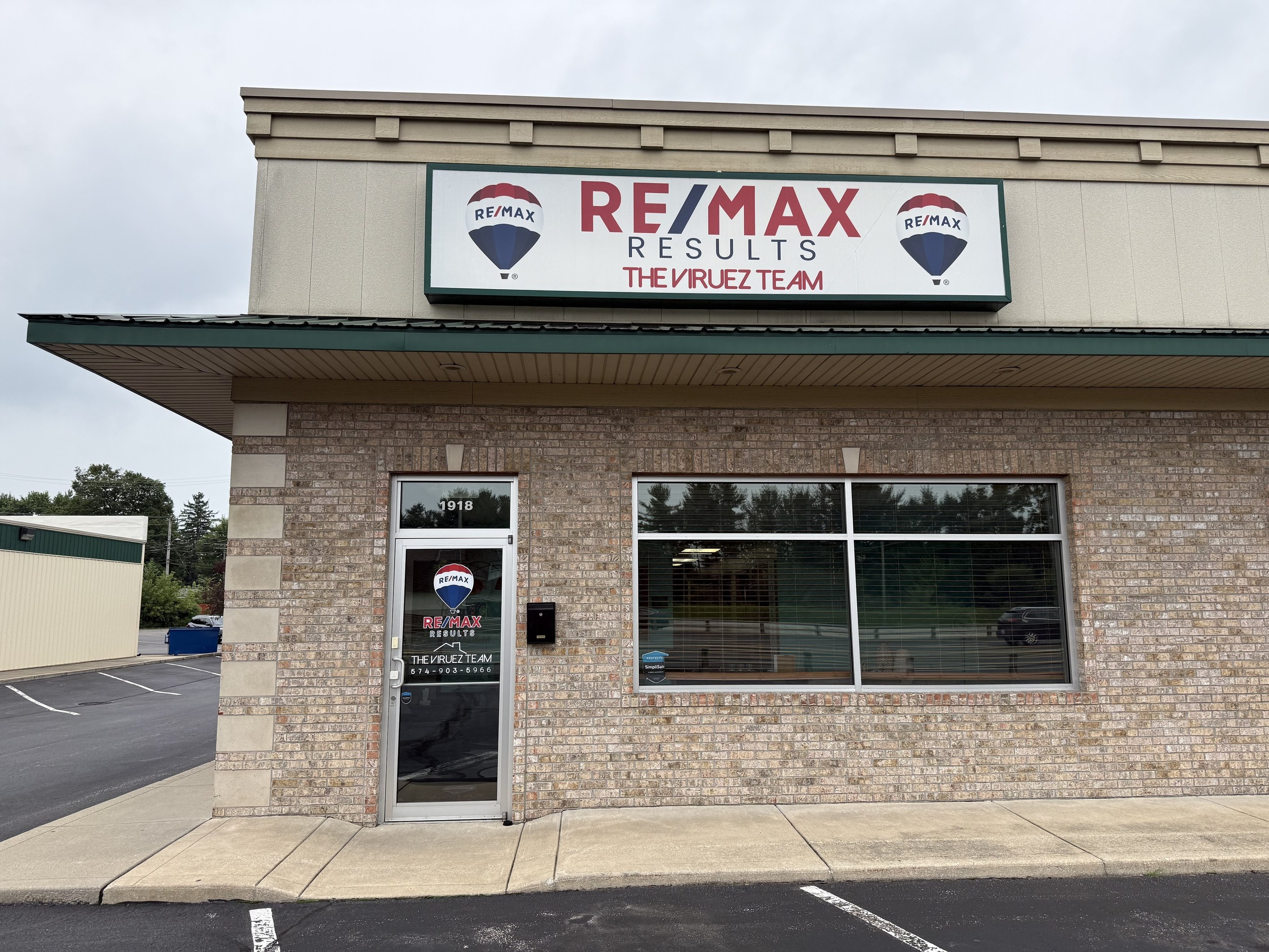 The RE/MAX Results, The Viruez Team office, a one-story brick storefront with a large RE/MAX sign above the entrance.
