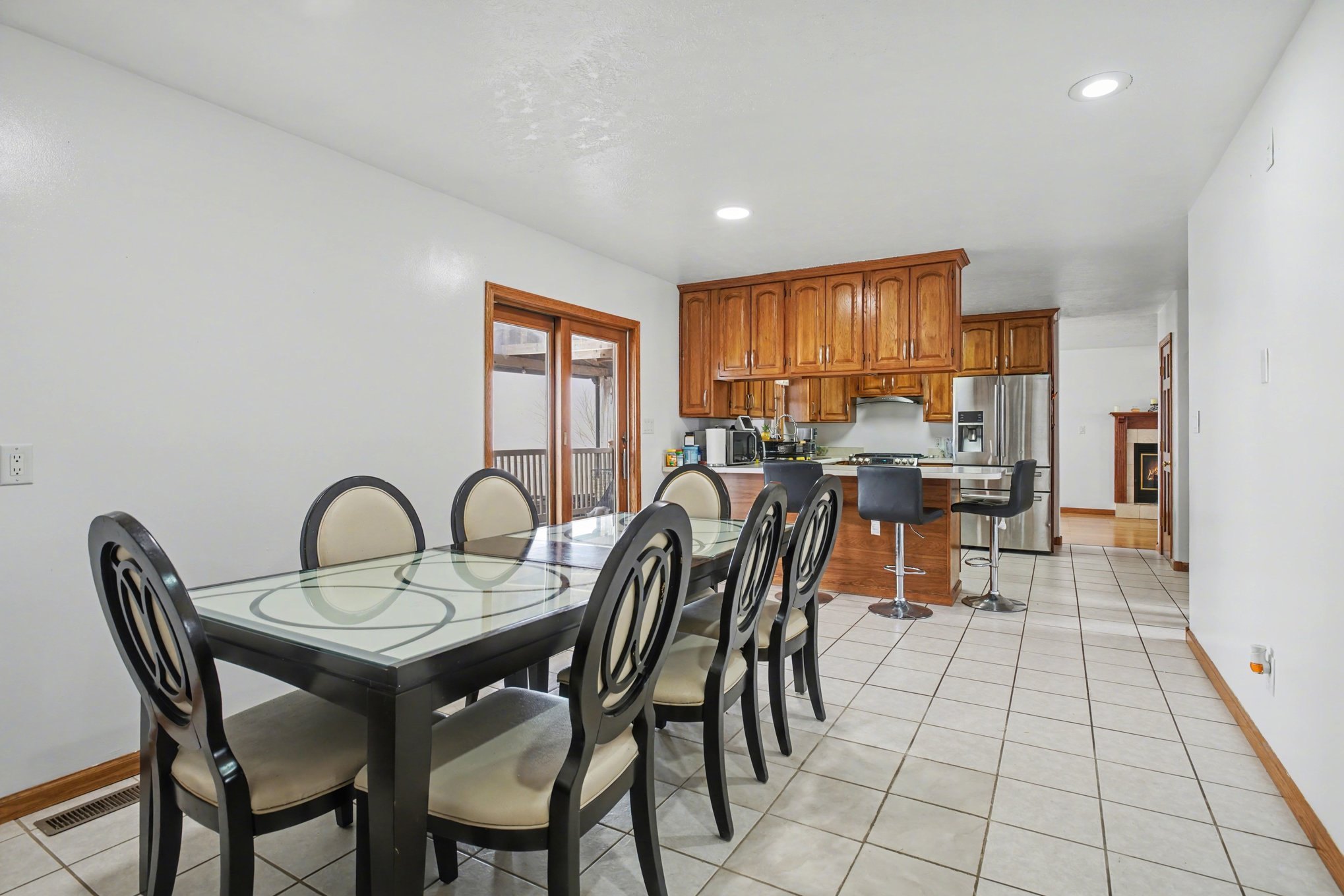 A bright open kitchen and dining area with a glass table, oak cabinets, and a stainless refrigerator.