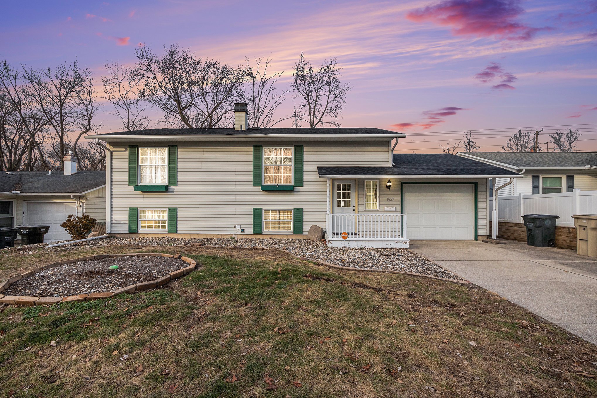 A split-level home with green shutters and a landscaped yard at dusk.