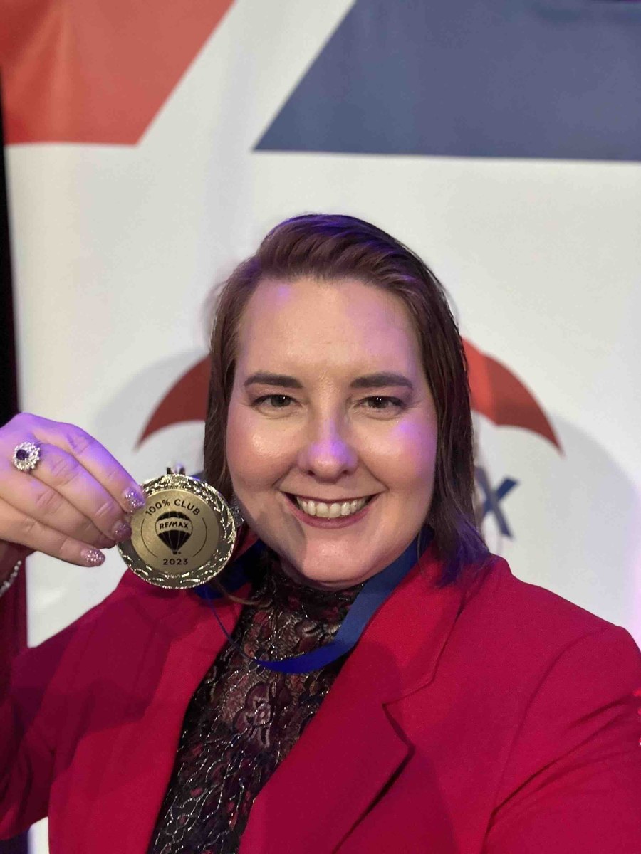 Lisa Collio holding her RE/MAX 100% Club award medal at a RE/MAX recognition event.