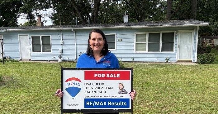 Lisa Collio standing beside a RE/MAX Results, The Viruez Team for-sale sign in front of a listed home.
