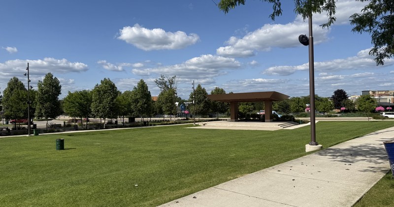 An open park lawn with a covered pavilion in the middle distance and a paved path along one side.