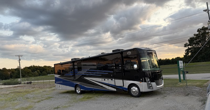 A motorhome parked on gravel at dusk under a heavy, clouded sky.