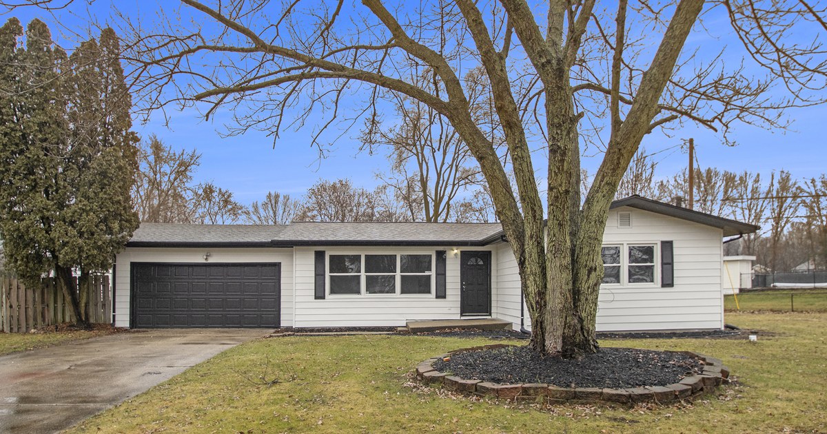 A single-storey house painted white with an attached garage and a bare tree on the front lawn in winter.