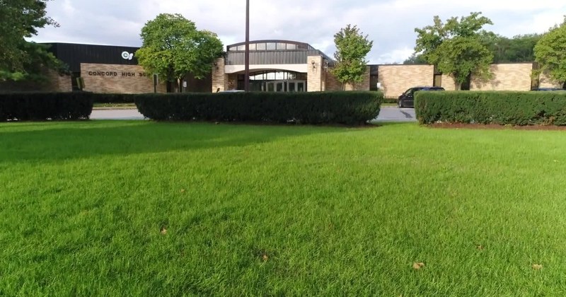A school building set behind a wide mown lawn and hedge.
