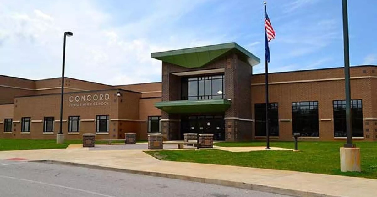 A Concord school building with flagpoles on a clear day.