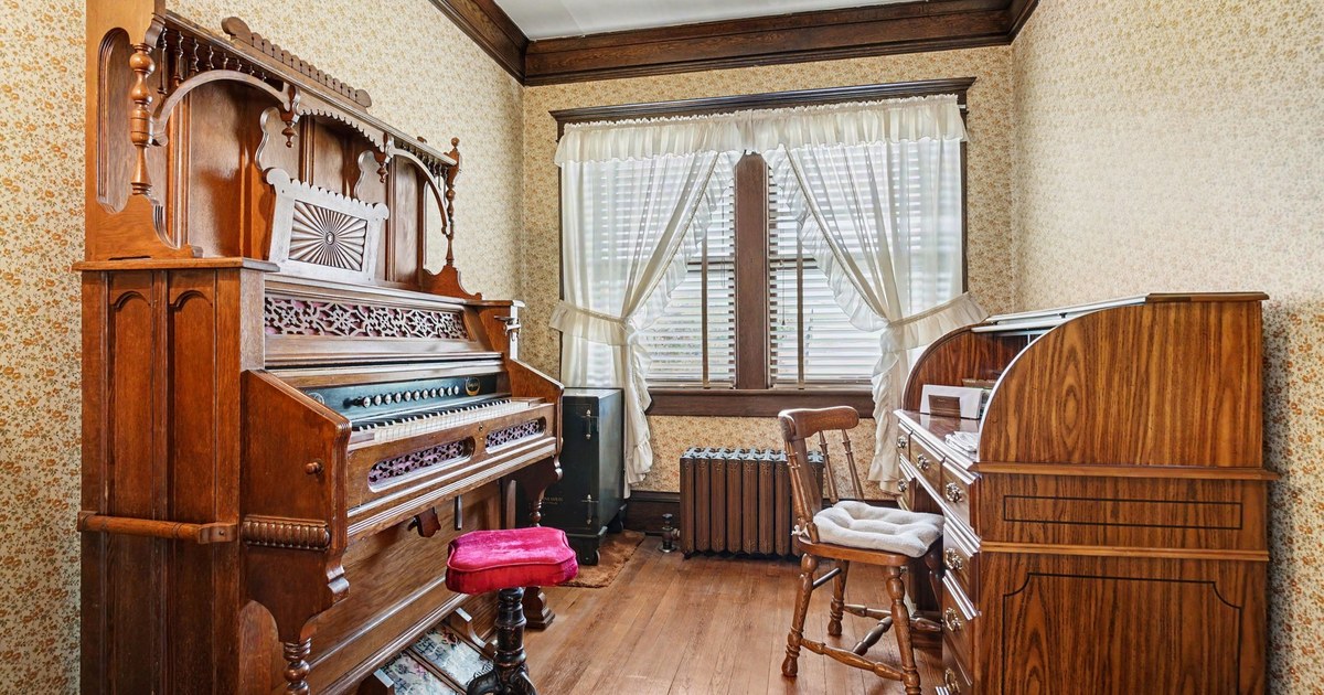 A parlour in an older home with a pump organ and lace curtains.