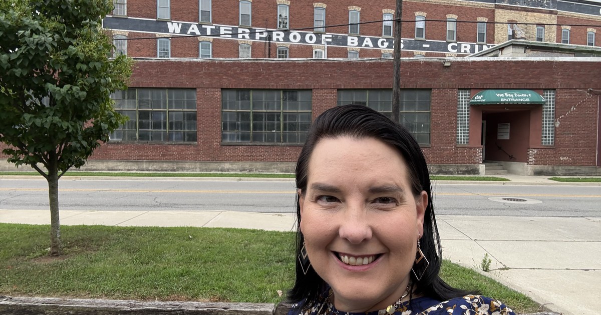 Lisa Collio outside a historic brick factory building in Goshen, Indiana, with painted Chase Bag Company signage on the facade.