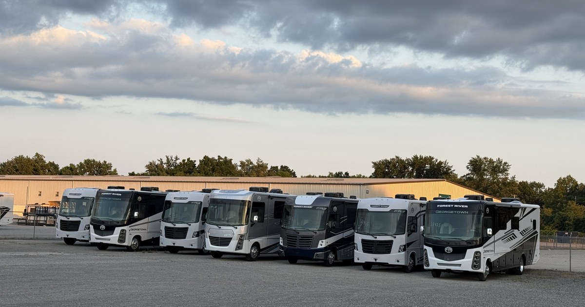 A row of new delivery vehicles lined up on a manufacturer's lot.