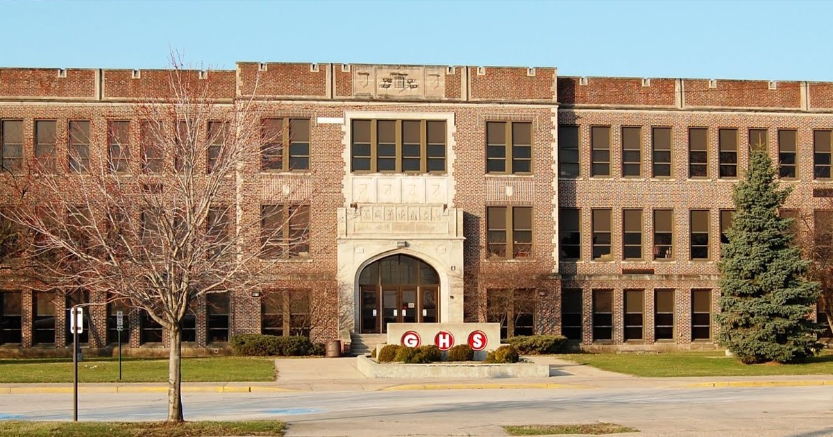 A large brick school building behind mature trees.